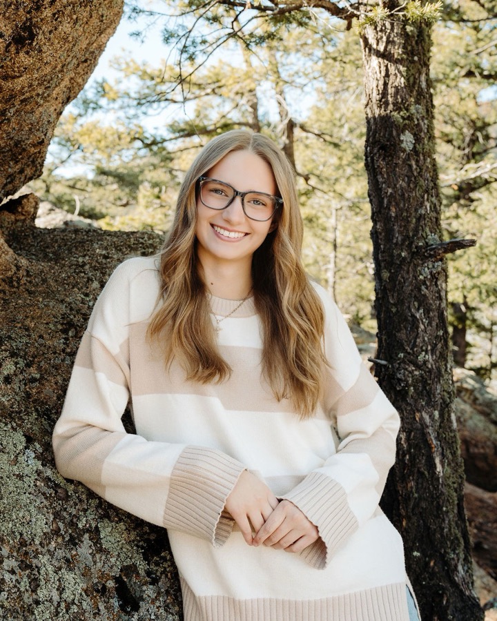 Megan Swearengin, esthetician, smiling outdoors among the Colorado pines